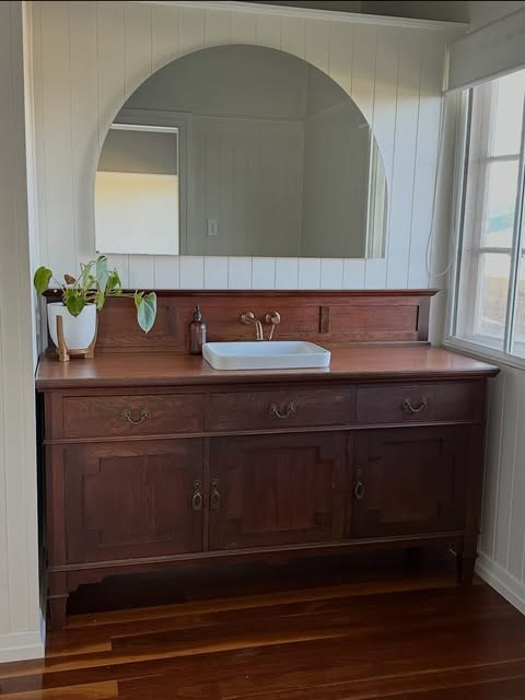 Restored timber vanity below an arched mirror, against vertical join panelling